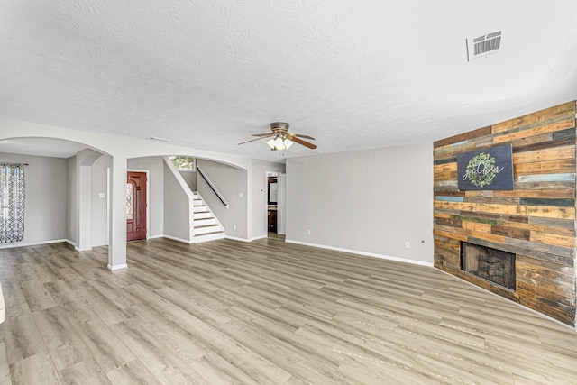 unfurnished living room featuring a large fireplace, visible vents, arched walkways, stairway, and light wood-style floors