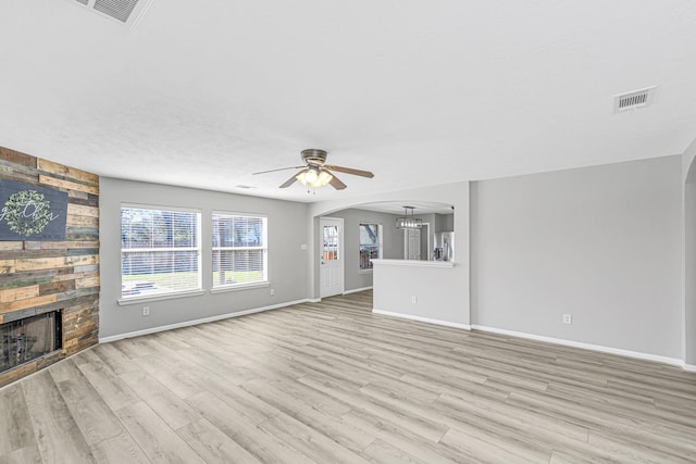 unfurnished living room with light wood-style floors, arched walkways, visible vents, and a fireplace