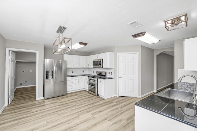 kitchen featuring decorative backsplash, dark countertops, appliances with stainless steel finishes, light wood-style floors, and a sink