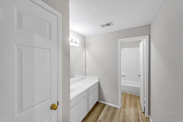 bathroom with a textured ceiling, wood finished floors, visible vents, vanity, and baseboards