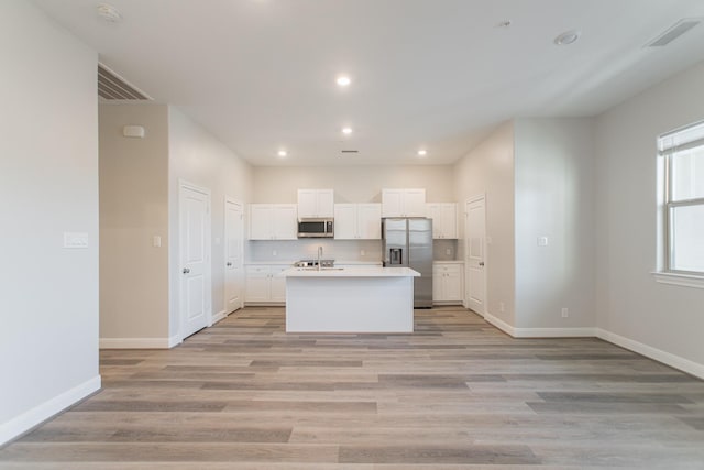 kitchen featuring stainless steel appliances, a kitchen island with sink, white cabinetry, and light wood finished floors