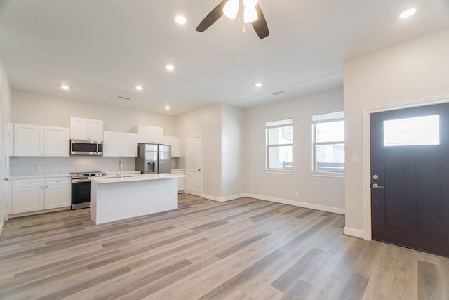 kitchen with stainless steel appliances, white cabinets, light wood-style floors, light countertops, and an island with sink