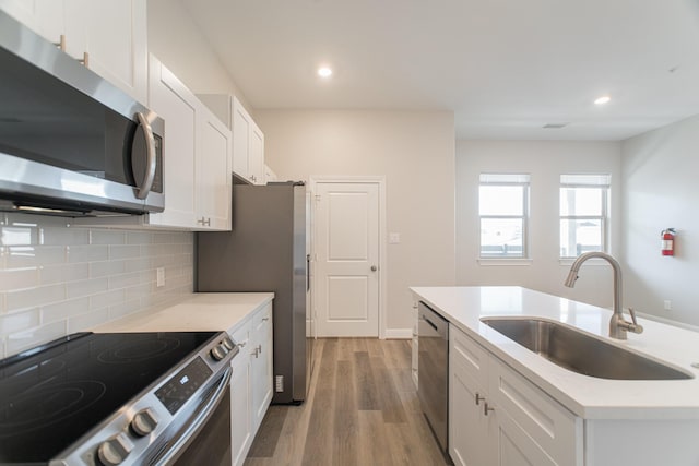 kitchen with a sink, white cabinetry, appliances with stainless steel finishes, light wood-type flooring, and tasteful backsplash