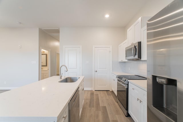 kitchen featuring a sink, light wood-style floors, appliances with stainless steel finishes, decorative backsplash, and an island with sink