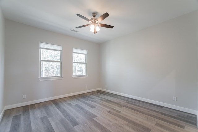 empty room featuring a ceiling fan, wood finished floors, visible vents, and baseboards