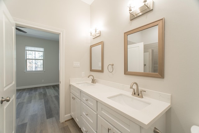 full bath with double vanity, wood finished floors, a sink, and baseboards