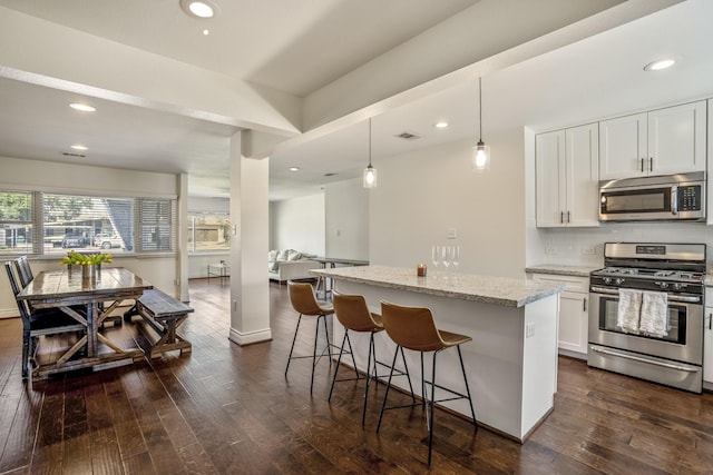 kitchen with a kitchen bar, a kitchen island, dark wood-style floors, stainless steel appliances, and light stone countertops