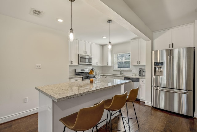 kitchen featuring visible vents, dark wood-type flooring, a center island, appliances with stainless steel finishes, and decorative backsplash