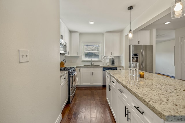 kitchen with light stone countertops, a sink, decorative backsplash, dark wood-type flooring, and stainless steel appliances