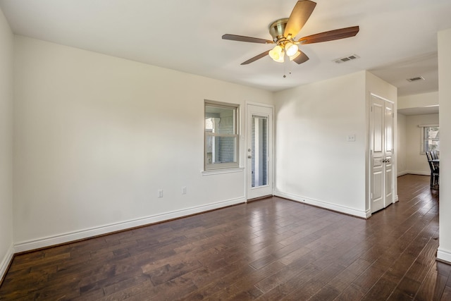 unfurnished room with dark wood-style floors, visible vents, ceiling fan, and baseboards