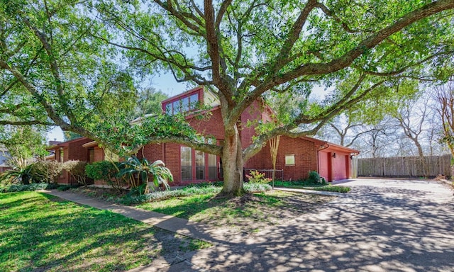 view of home's exterior with a lawn, driveway, fence, an attached garage, and brick siding