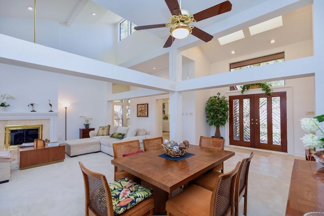 dining room featuring a skylight, a high ceiling, ceiling fan, french doors, and a tiled fireplace