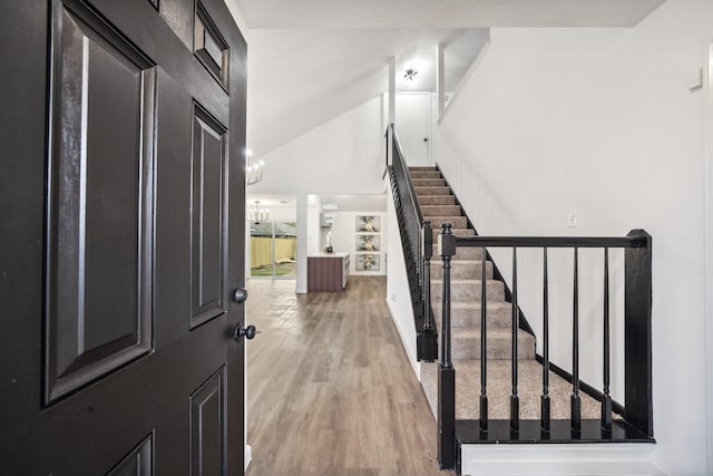 entryway featuring high vaulted ceiling, light wood-style flooring, and stairway