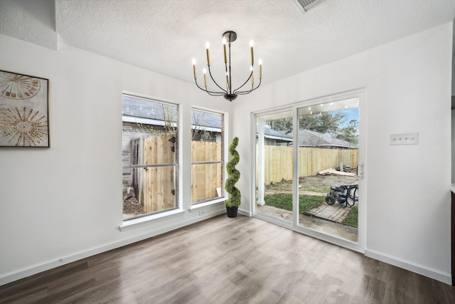 unfurnished dining area featuring baseboards, a textured ceiling, a chandelier, and wood finished floors