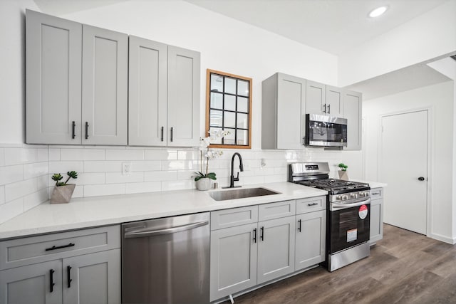 kitchen with gray cabinetry, dark wood-type flooring, a sink, appliances with stainless steel finishes, and decorative backsplash