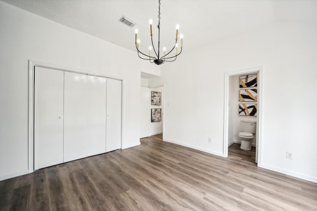 unfurnished bedroom with a closet, visible vents, an inviting chandelier, and wood finished floors