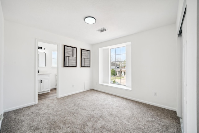 unfurnished bedroom with carpet, visible vents, baseboards, and ensuite bathroom