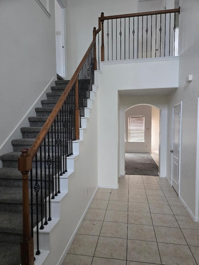 stairway with tile patterned flooring, baseboards, arched walkways, and a towering ceiling