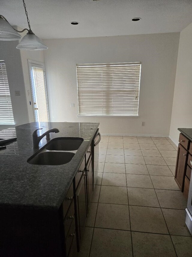 kitchen with tile patterned flooring, dishwasher, dark stone counters, hanging light fixtures, and a sink