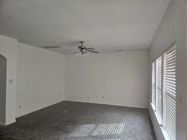 unfurnished room with dark colored carpet, visible vents, baseboards, and ceiling fan