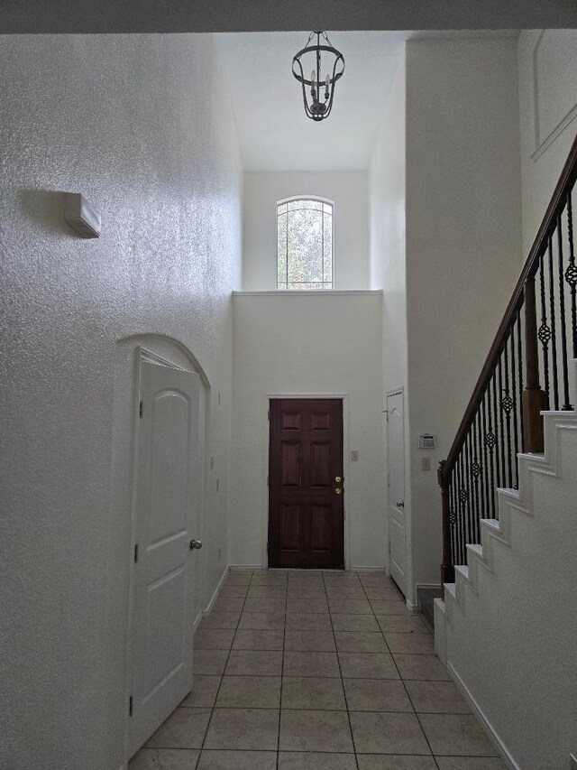 foyer entrance featuring stairway, light tile patterned floors, baseboards, a towering ceiling, and a chandelier