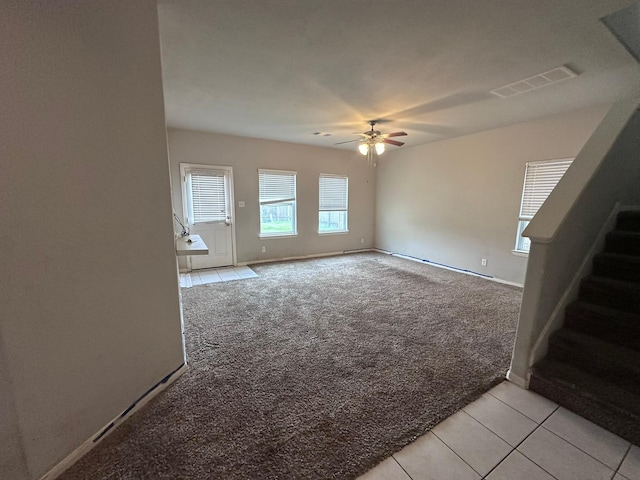 unfurnished room featuring light tile patterned floors, visible vents, light colored carpet, ceiling fan, and stairway