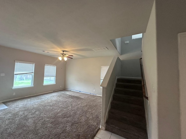 interior space featuring light carpet, visible vents, baseboards, ceiling fan, and stairway