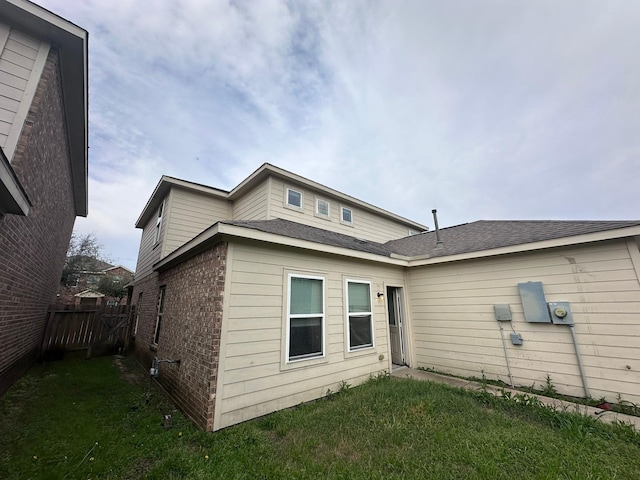 rear view of property featuring brick siding, a yard, and fence