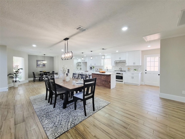 dining area with light wood-type flooring, visible vents, a textured ceiling, and baseboards