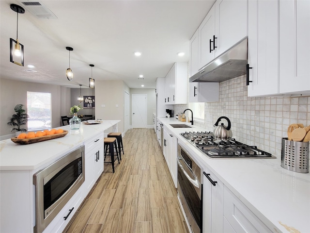 kitchen featuring a breakfast bar, stainless steel appliances, light wood-style floors, a sink, and under cabinet range hood