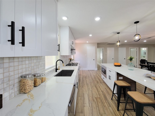 kitchen featuring stainless steel appliances, light stone counters, a sink, and white cabinetry