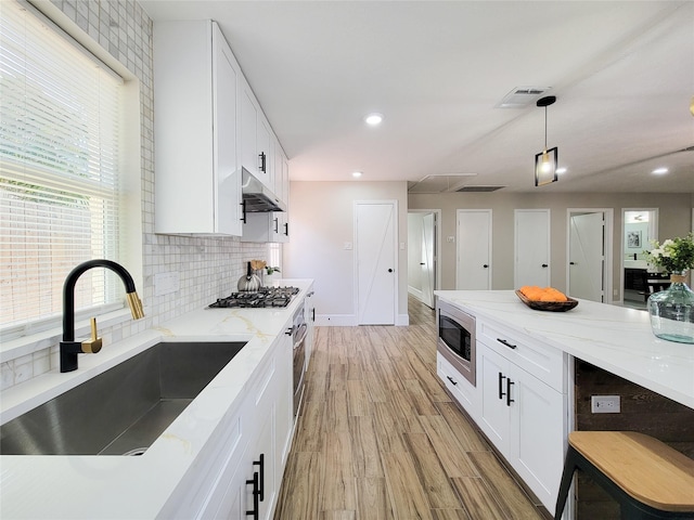 kitchen with light wood finished floors, appliances with stainless steel finishes, under cabinet range hood, white cabinetry, and a sink