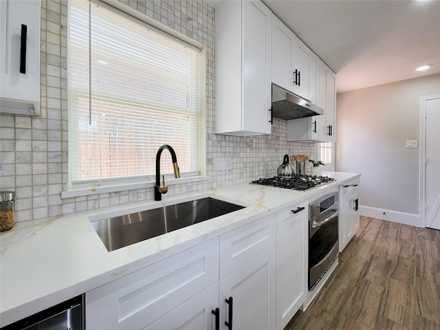 kitchen featuring appliances with stainless steel finishes, wood finished floors, under cabinet range hood, white cabinetry, and a sink