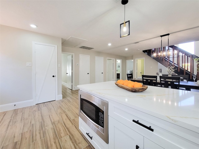 kitchen with visible vents, light stone countertops, light wood finished floors, stainless steel microwave, and pendant lighting