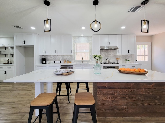 kitchen with stainless steel dishwasher, a large island, visible vents, and under cabinet range hood