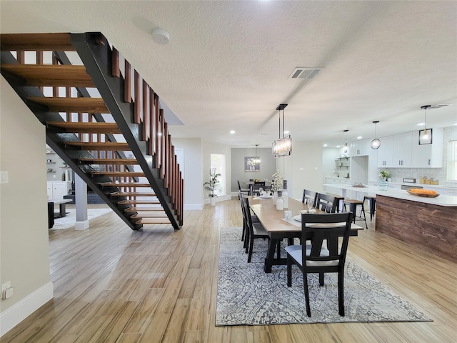 dining room featuring light wood finished floors, stairway, visible vents, and a textured ceiling