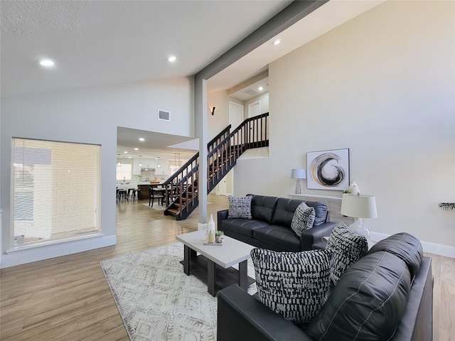 living room featuring high vaulted ceiling, wood finished floors, visible vents, and stairs