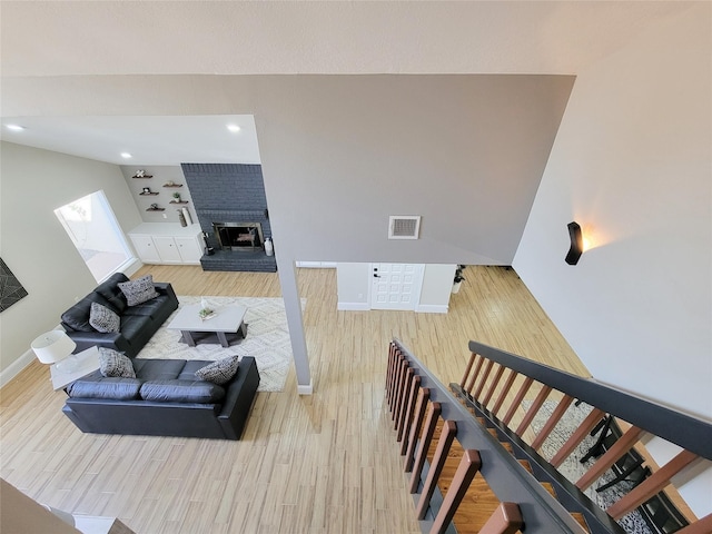 living area featuring baseboards, visible vents, stairway, wood finished floors, and a fireplace