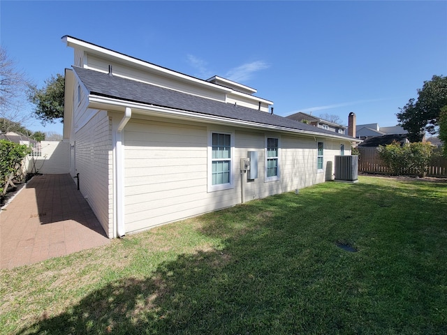 back of house with central AC, a lawn, fence, and roof with shingles