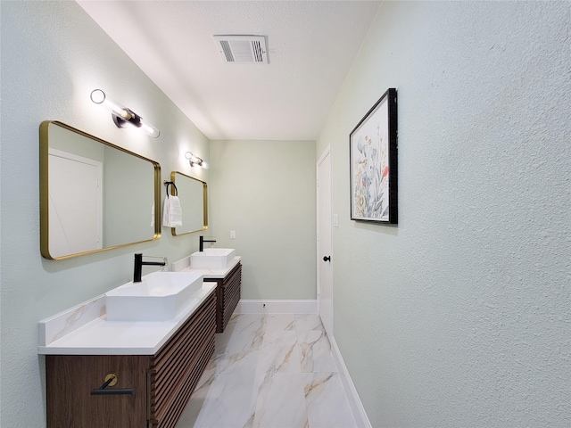 bathroom with marble finish floor, double vanity, visible vents, a sink, and baseboards