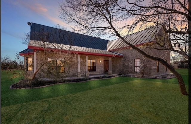 view of front facade featuring a standing seam roof, a yard, metal roof, and brick siding