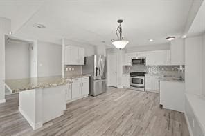 kitchen with white cabinets, light wood-style flooring, stainless steel appliances, and backsplash