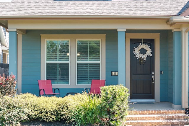 doorway to property with a shingled roof and a porch