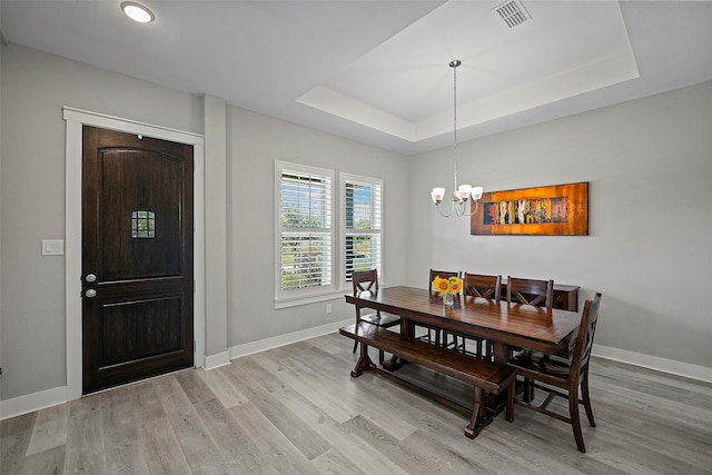 dining space with baseboards, a raised ceiling, visible vents, and light wood-style floors