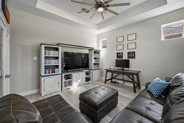 living room with ceiling fan, a raised ceiling, light wood-style flooring, and baseboards