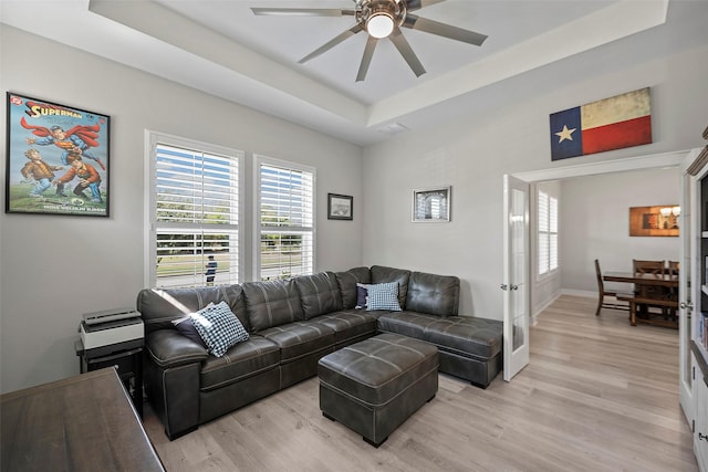 living area with french doors, light wood finished floors, a raised ceiling, and a ceiling fan