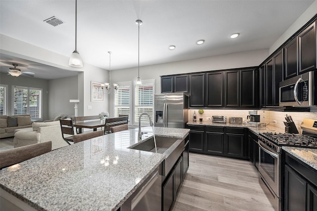 kitchen with visible vents, decorative backsplash, appliances with stainless steel finishes, open floor plan, and a sink