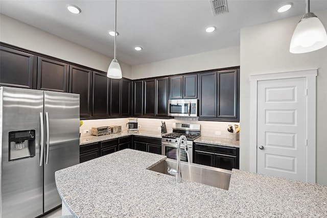 kitchen with stainless steel appliances, a sink, visible vents, light stone countertops, and tasteful backsplash