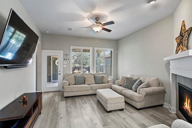 living room with a ceiling fan, light wood-type flooring, visible vents, and a lit fireplace