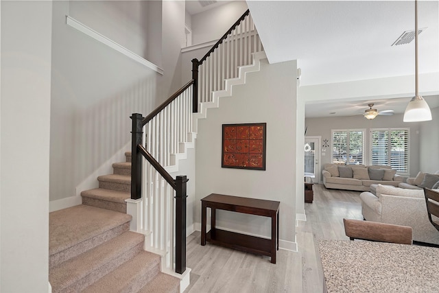 staircase with visible vents, a high ceiling, a ceiling fan, wood finished floors, and baseboards